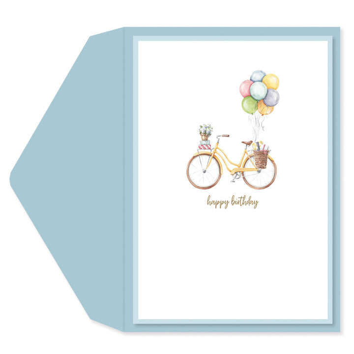 A square greeting card with a light blue envelope behind it. The card features a watercolor illustration of a yellow bicycle with a basket of colorful balloons and the words 'happy birthday' in gold script.