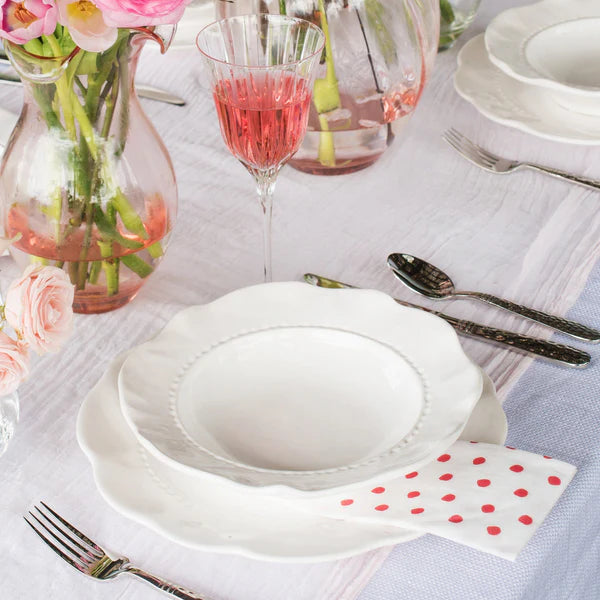 Elegant table setting with white plates, pink flowers, and red wine.