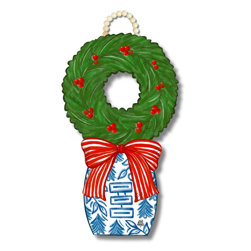 A Christmas wreath hanging ornament with a green wreath top, red berries, a red and white striped bow, and a blue and white patterned base, hanging from a cream beaded loop.