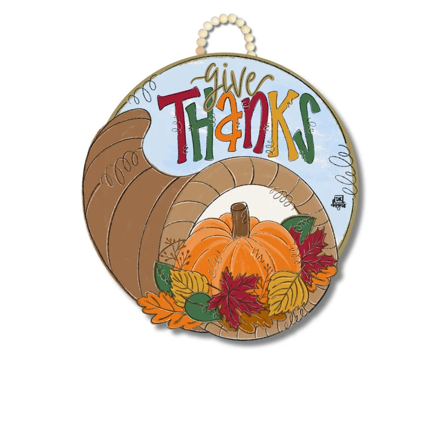 A round decorative hanging sign featuring a Thanksgiving harvest design. The sign shows a brown cornucopia with the words “give thanks,” orange pumpkins, and autumn leaves on a white background.