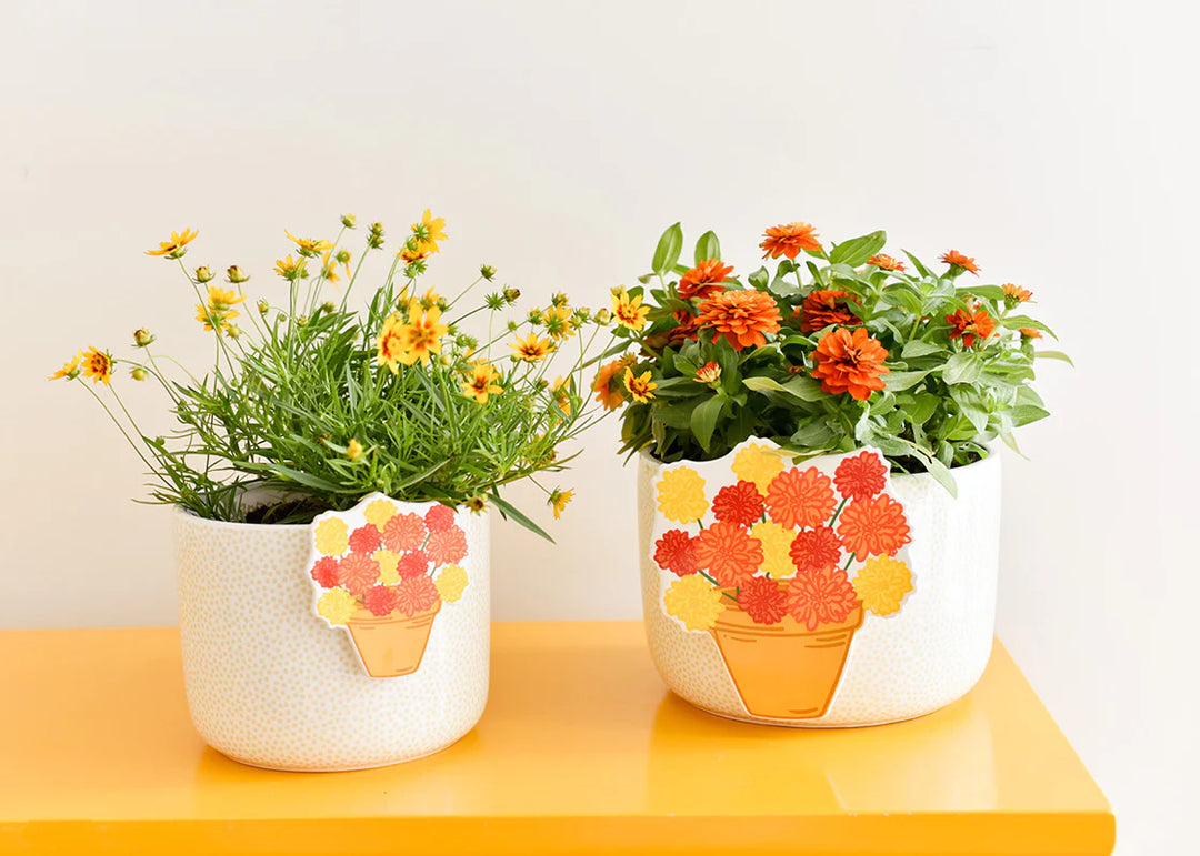 Two decorative planters with floral designs on a yellow surface against a white background