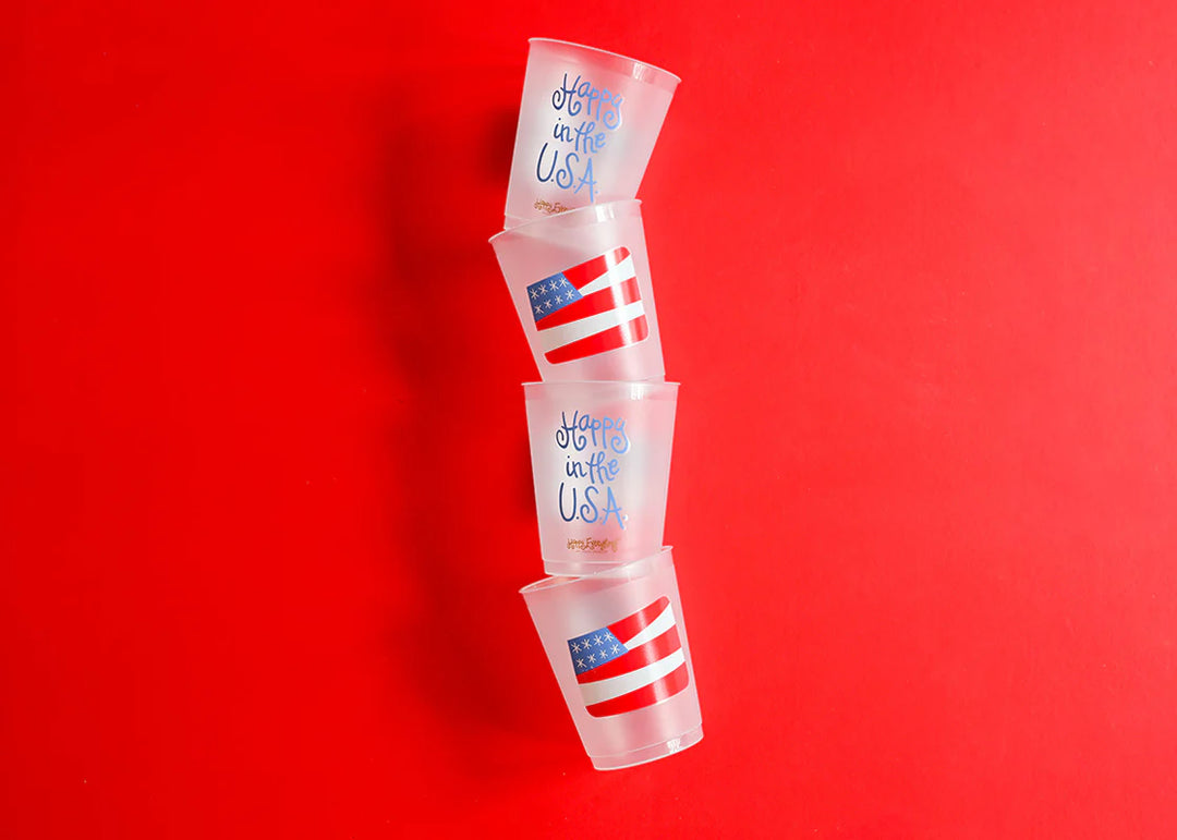 STACK OF FROSTED PLASTIC CUPS WITH FROSTED PLASTIC CUP WITH AMERICAN FLAG PRINTED ON IT AND HAPPY IN THE USA ON RED BACKGROUND
