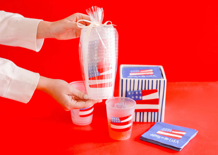 STACK OF FROSTED PLASTIC CUPS WITH FROSTED PLASTIC CUP WITH AMERICAN FLAG PRINTED ON IT AND HAPPY IN THE USA ON RED BACKGROUND