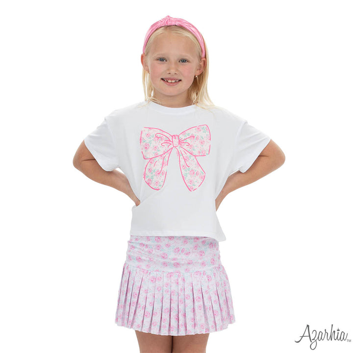 Young girl wearing a white t-shirt with a pink bow design and a matching skirt on a white background.