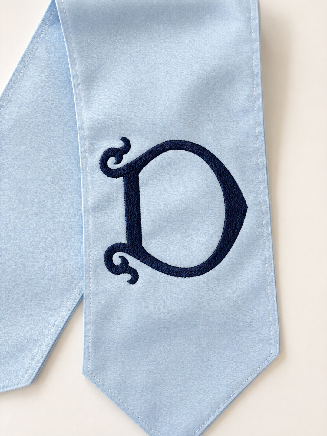 Light blue fabric with a navy embroidered letter 'D' on a beige background