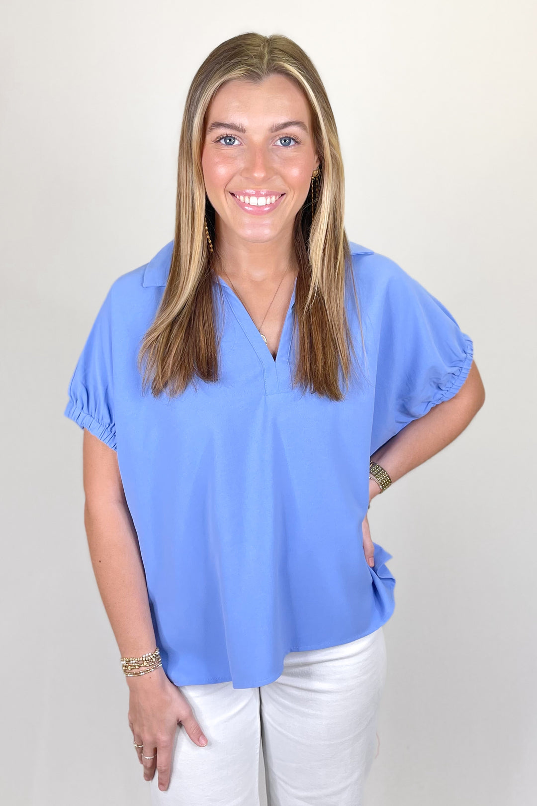 Woman modeling a solid blue short sleeve blouse with collared V-neckline and white pants.