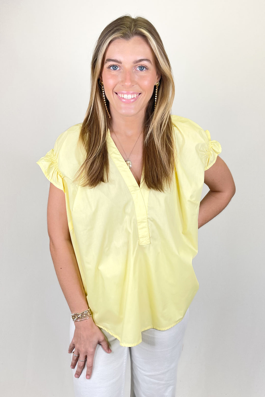 Woman modeling a light yellow short sleeve blouse with split neckline and gathered sleeve detail paired with white pants.