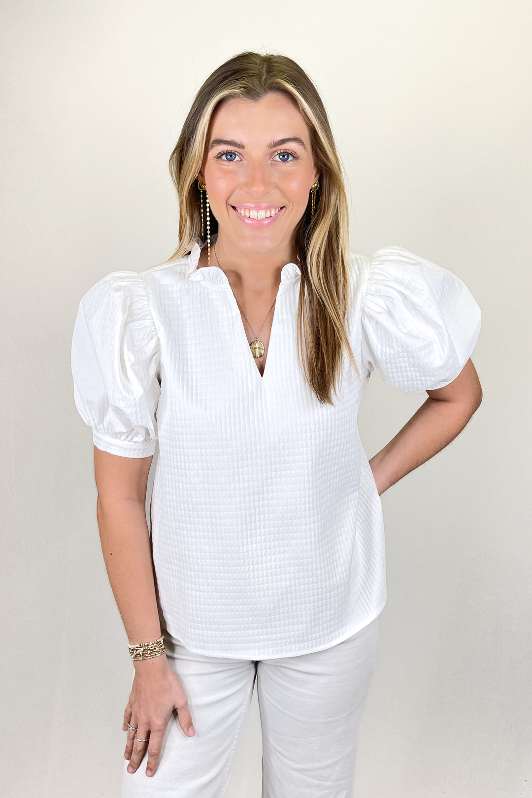 Woman modeling a white textured blouse with puff sleeves and split ruffle neckline paired with white pants.