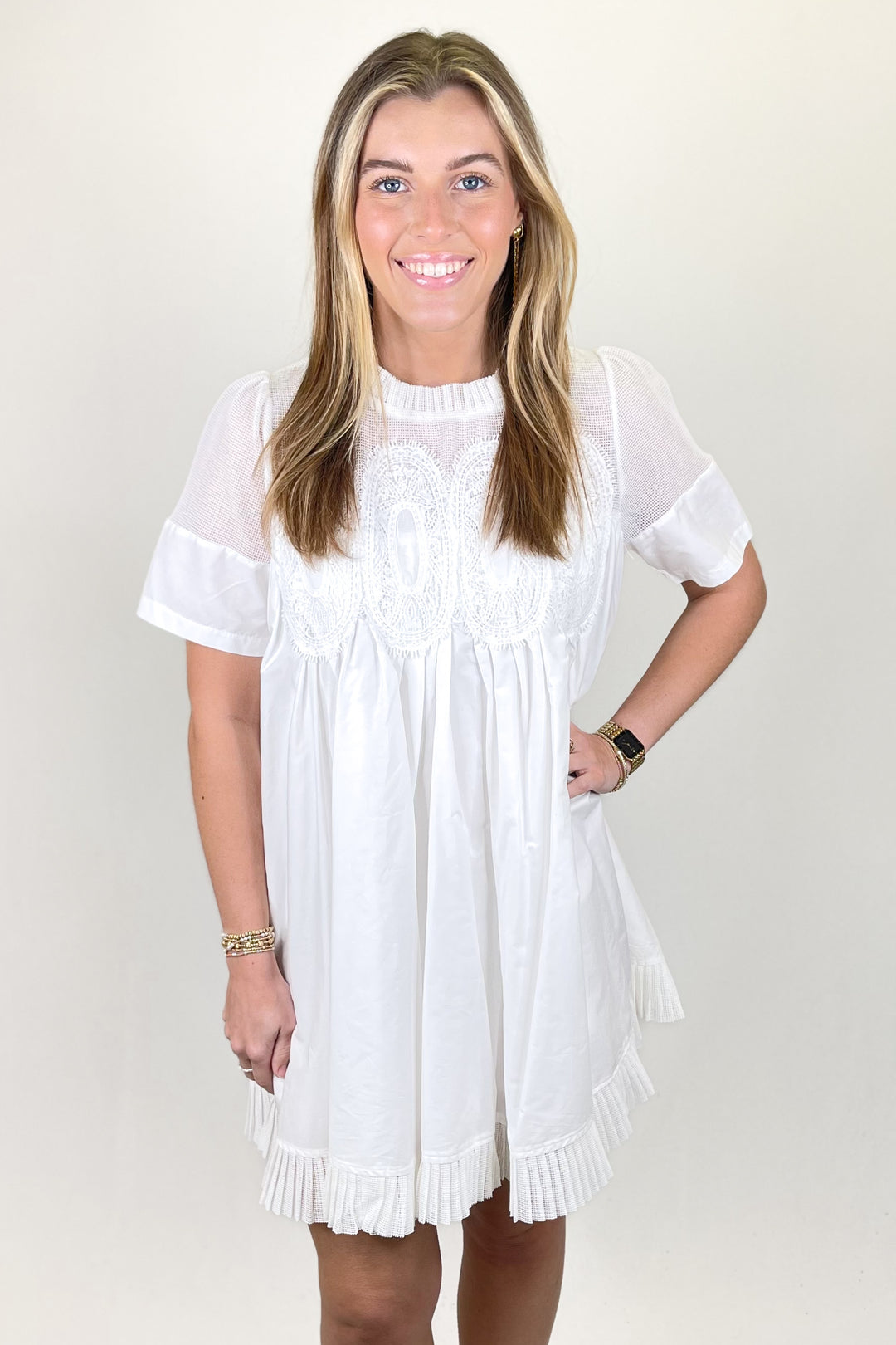 Woman modeling a white short sleeve dress with lace detail, sheer yoke, and pleated ruffle hem.