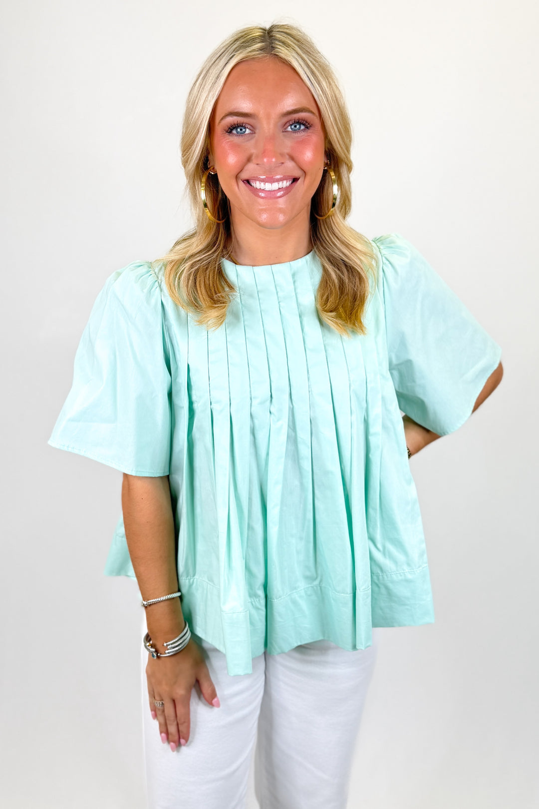 Woman wearing a mint pleated top with white pants.