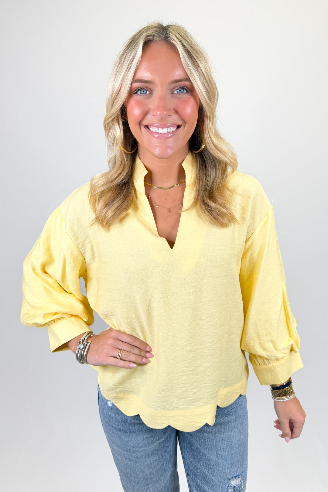 Yellow long sleeve blouse with scalloped hem, split neckline, and relaxed fit paired with denim