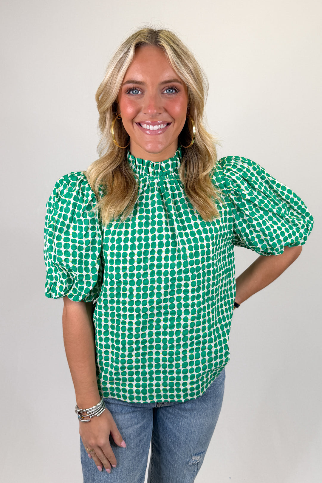Green and white dot print blouse with puff sleeves, high ruffle neckline, and relaxed fit
