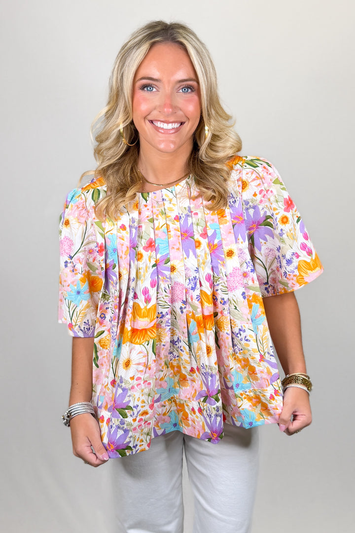 Multicolor floral blouse for women with short sleeves and flowy pleated silhouette styled with white pants