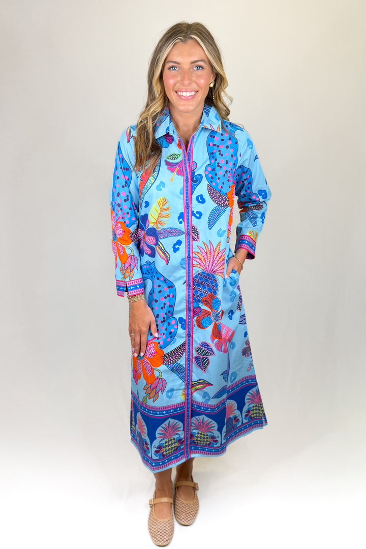 Blue floral print midi dress with long sleeves, collared neckline, button front, and colorful border detail, featuring pockets and a relaxed fit