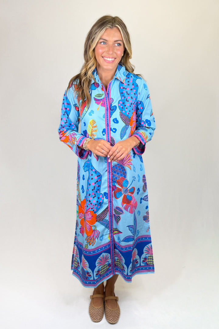 Blue floral print midi dress with long sleeves, collared neckline, button front, and colorful border detail, featuring pockets and a relaxed fit