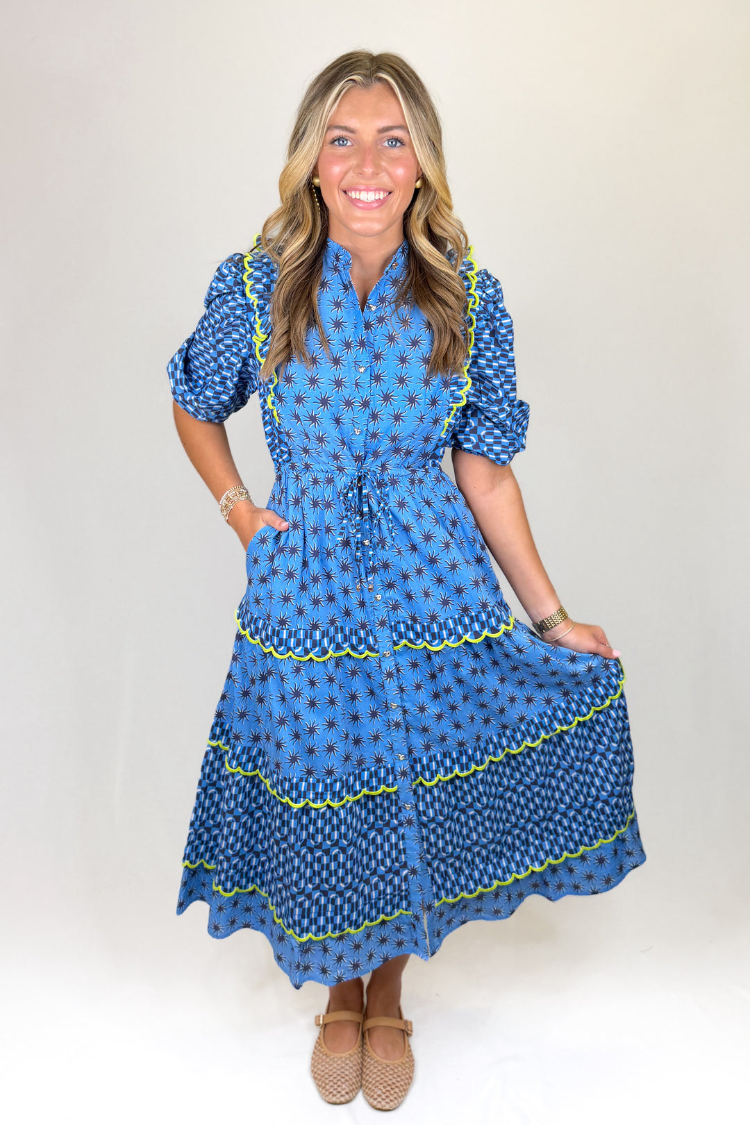 Blue patterned midi dress with short puff sleeves, collared neckline, button front, and drawstring waist, featuring tiered skirt with contrast trim and a flowy fit