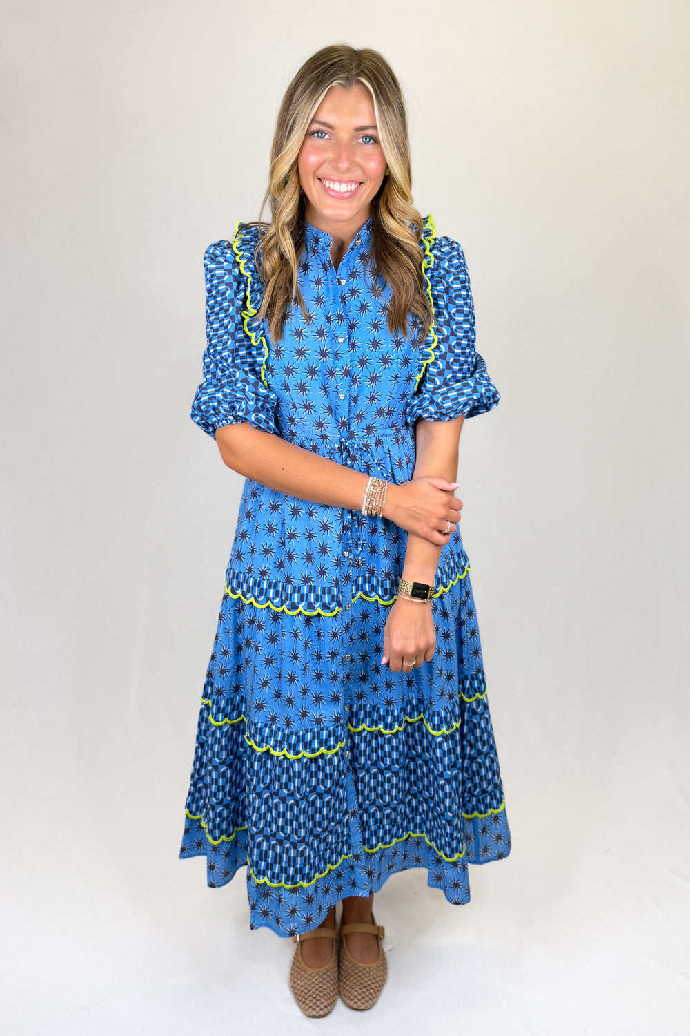 Blue patterned midi dress with short puff sleeves, collared neckline, button front, and drawstring waist, featuring tiered skirt with contrast trim and a flowy fit