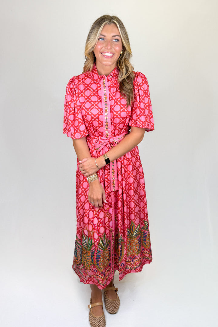 Pink patterned midi dress with short puff sleeves, collared neckline, button front, and tie waist, featuring a contrast border hem, pockets, and a flowy fit