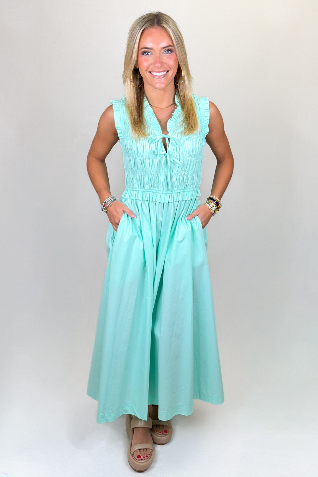 Aqua green maxi dress with ruffle neckline, sleeveless design, smocked bodice, and flowy skirt, featuring pockets and a lightweight feel