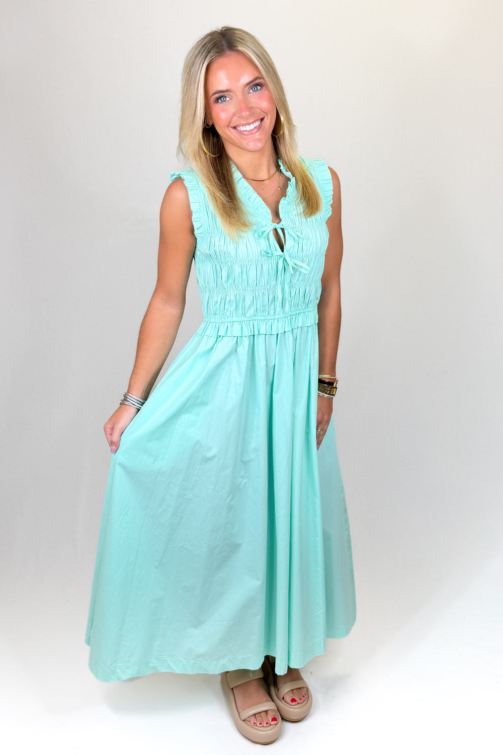 Aqua green maxi dress with ruffle neckline, sleeveless design, smocked bodice, and flowy skirt, featuring pockets and a lightweight feel