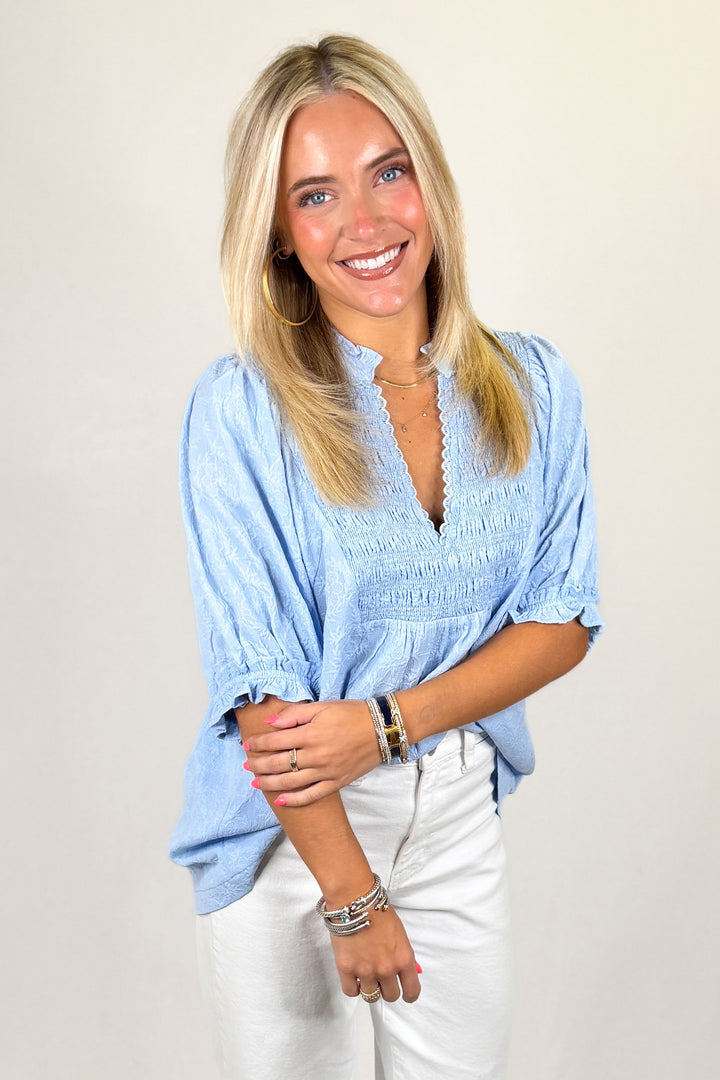 Light blue textured blouse with smocked bodice, puff sleeves, and scalloped neckline, women’s boutique top