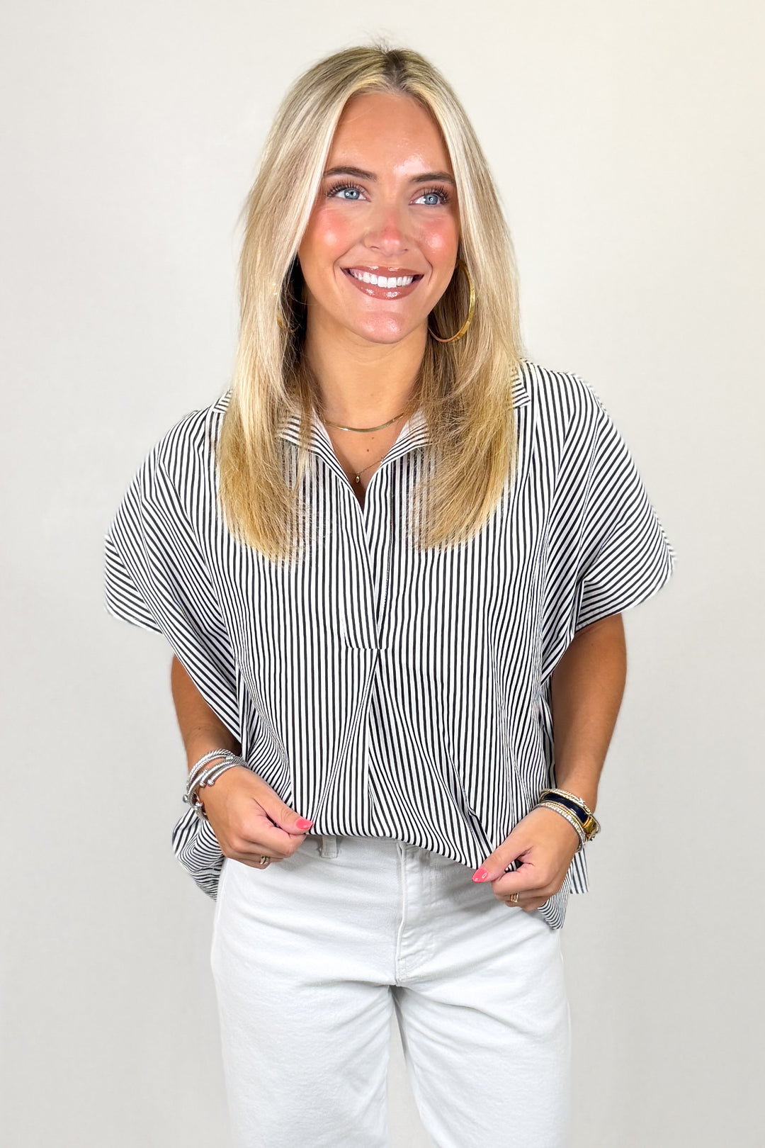 Woman wearing a black and white striped shirt with white pants on a plain background