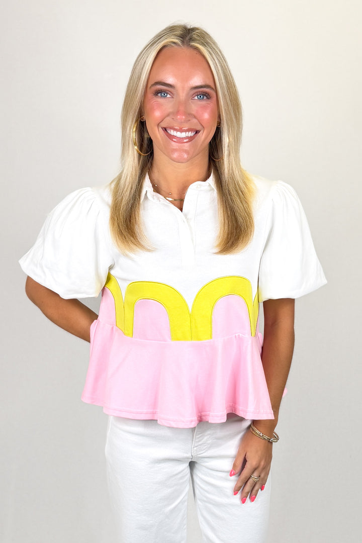 White top with puff sleeves and pink peplum hem with yellow scallop detail