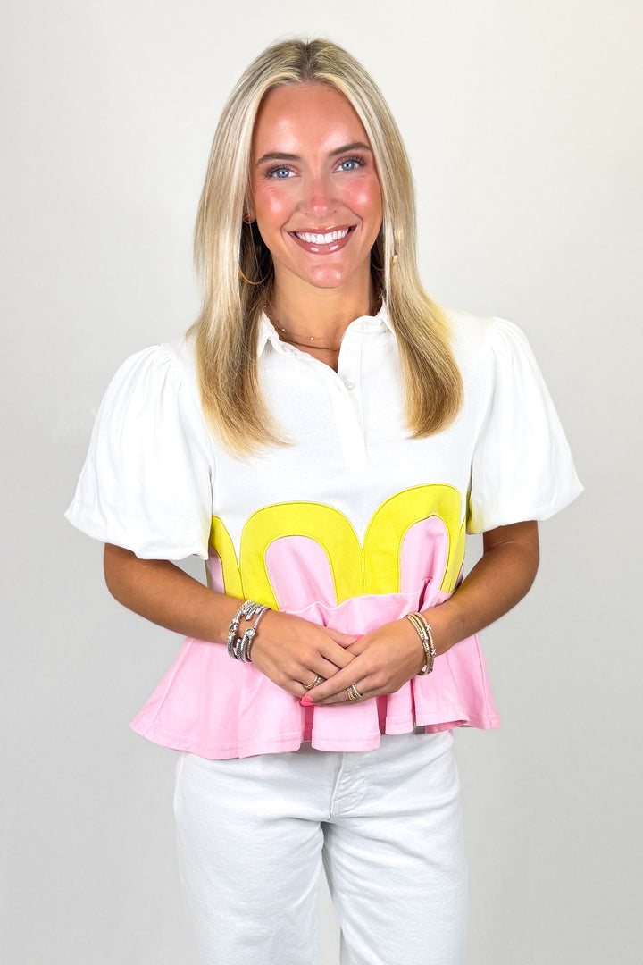 White top with puff sleeves and pink peplum hem with yellow scallop detail