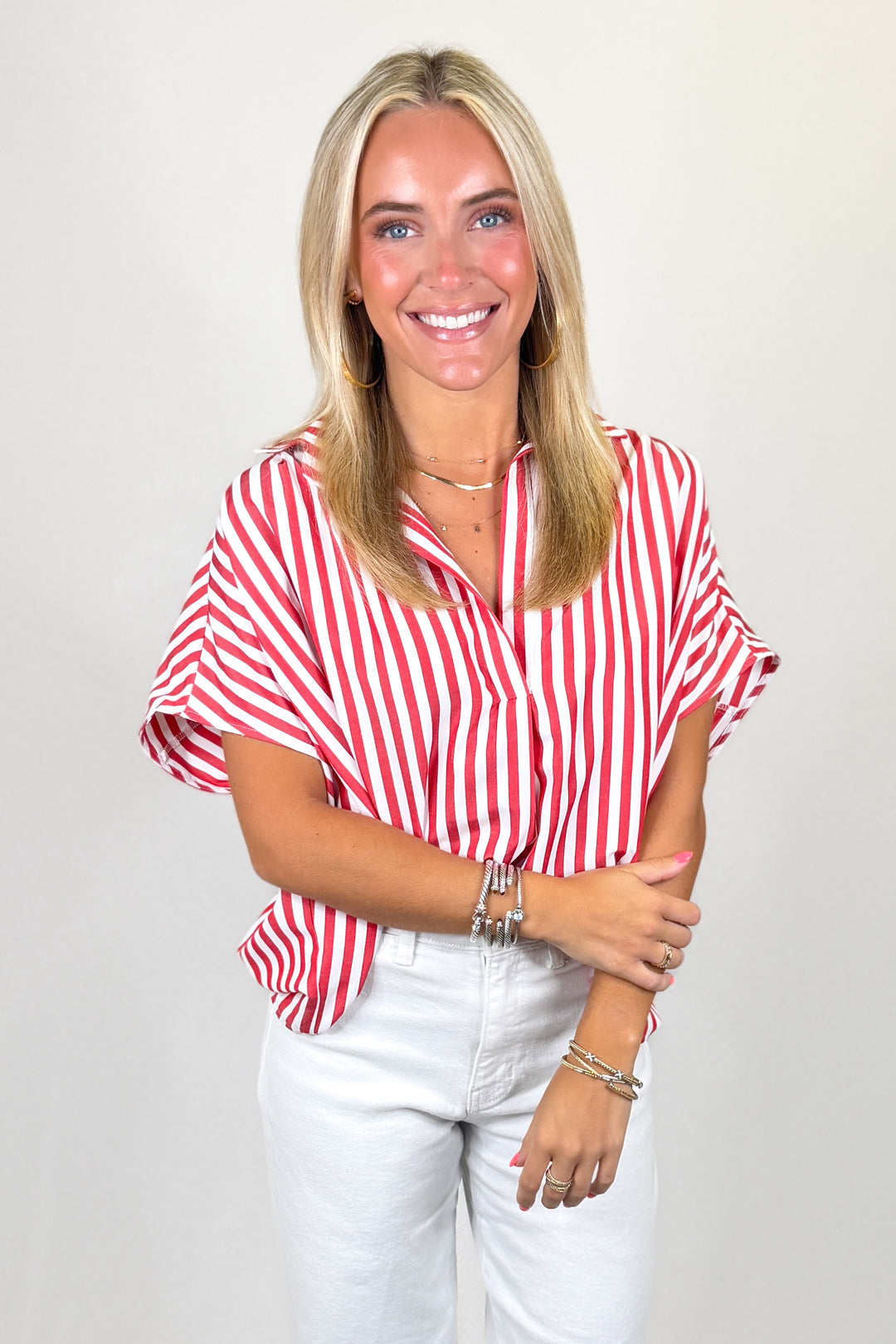 Red and white striped flutter sleeve blouse paired with white denim jeans and gold hoop earrings, styled for a bright summer boutique outfit.