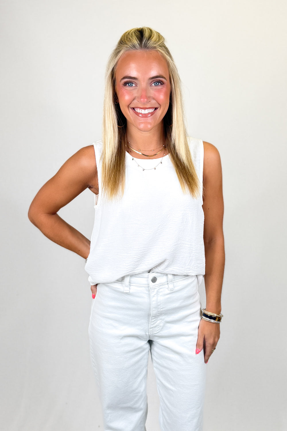 Woman wearing a white sleeveless top and light blue jeans against a plain background