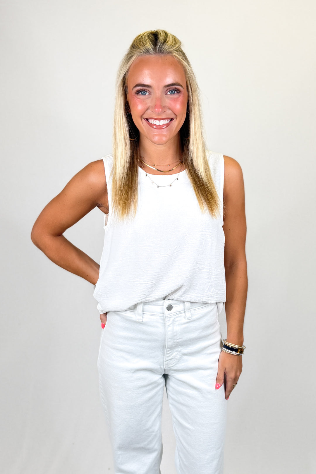 Woman wearing a white sleeveless top and light blue jeans against a plain background