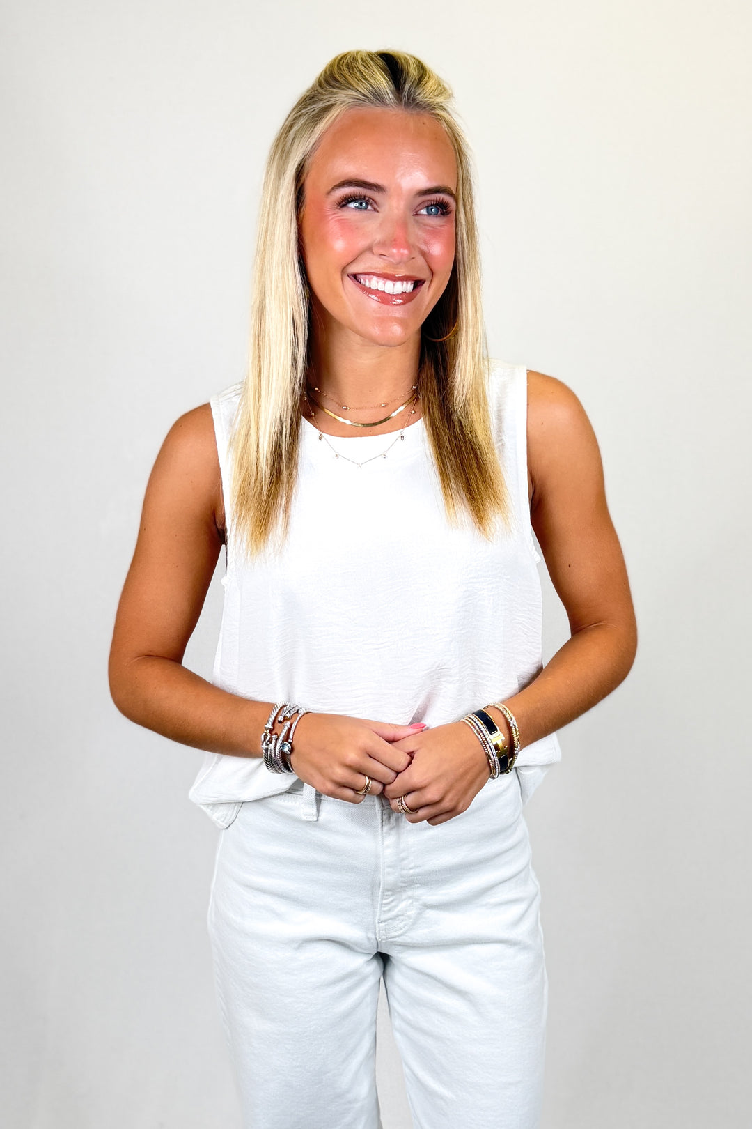 Woman wearing a white sleeveless top and light blue jeans against a plain background