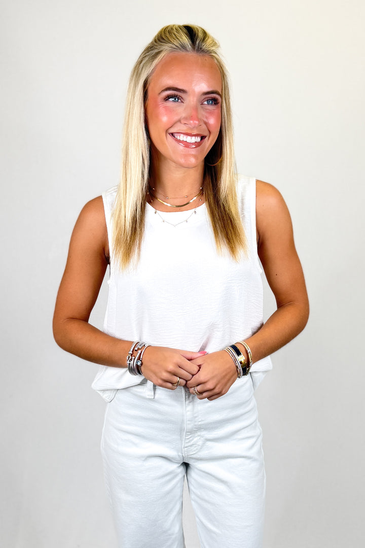 Woman wearing a white sleeveless top and light blue jeans against a plain background