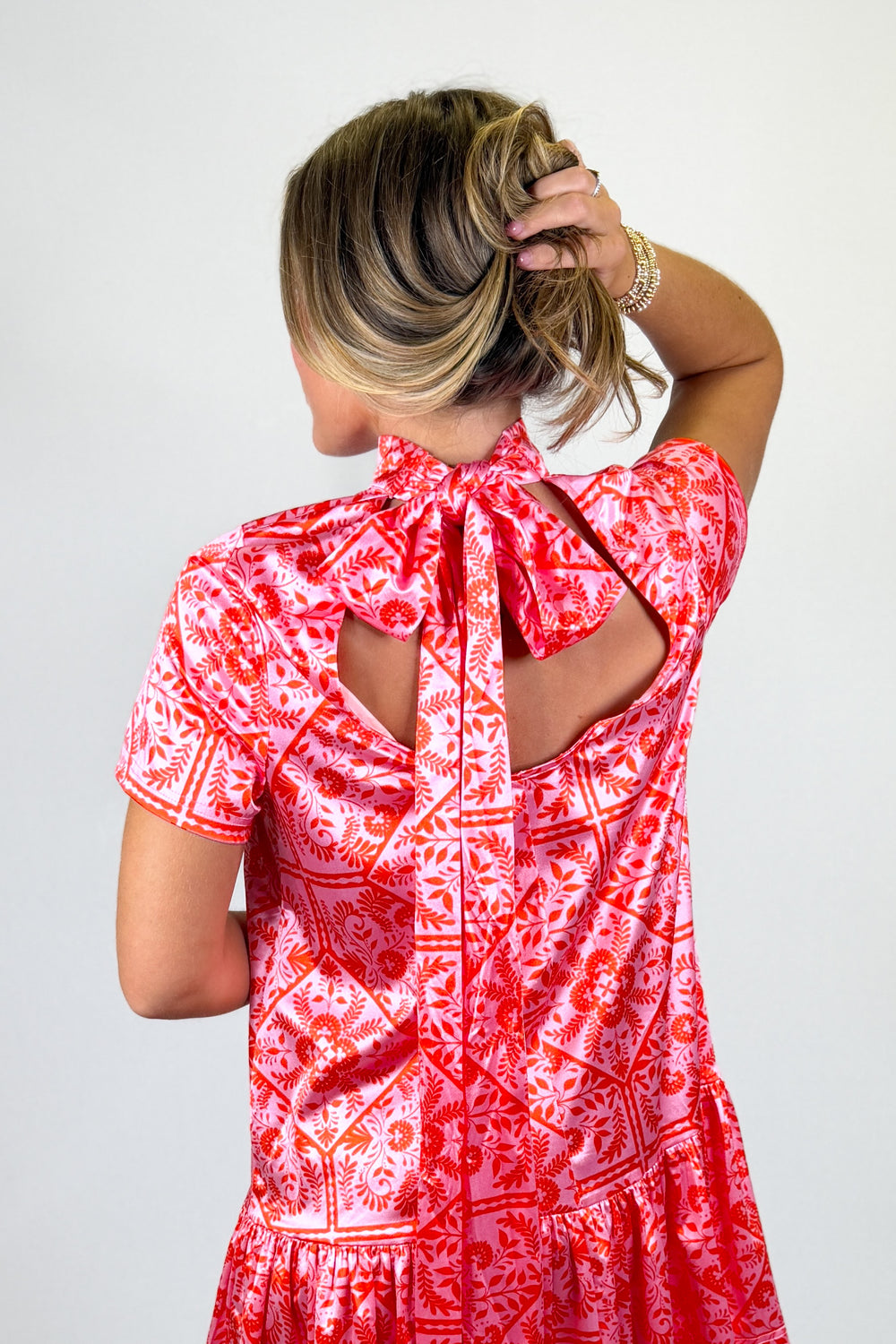 Woman wearing a red and white patterned dress with cut-out back on a plain background