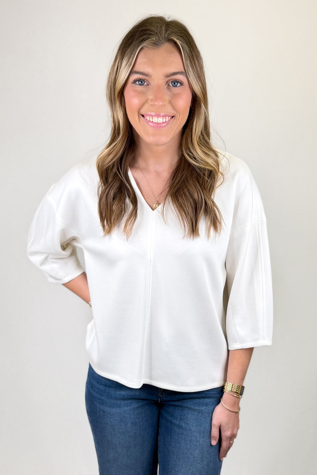 Woman wearing a white blouse and blue jeans against a plain background
