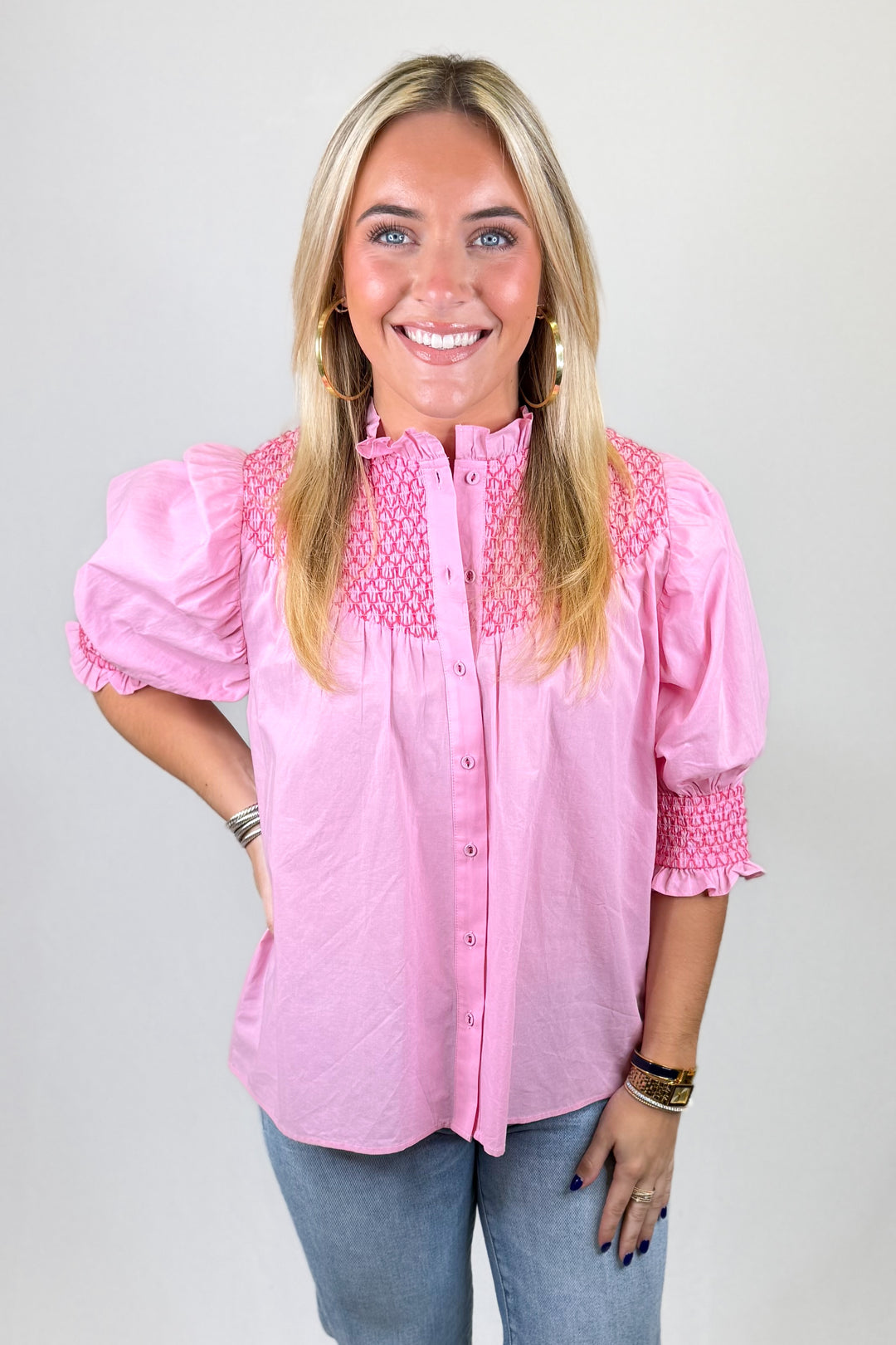 Woman wearing a pink blouse with ruffled sleeves against a plain background