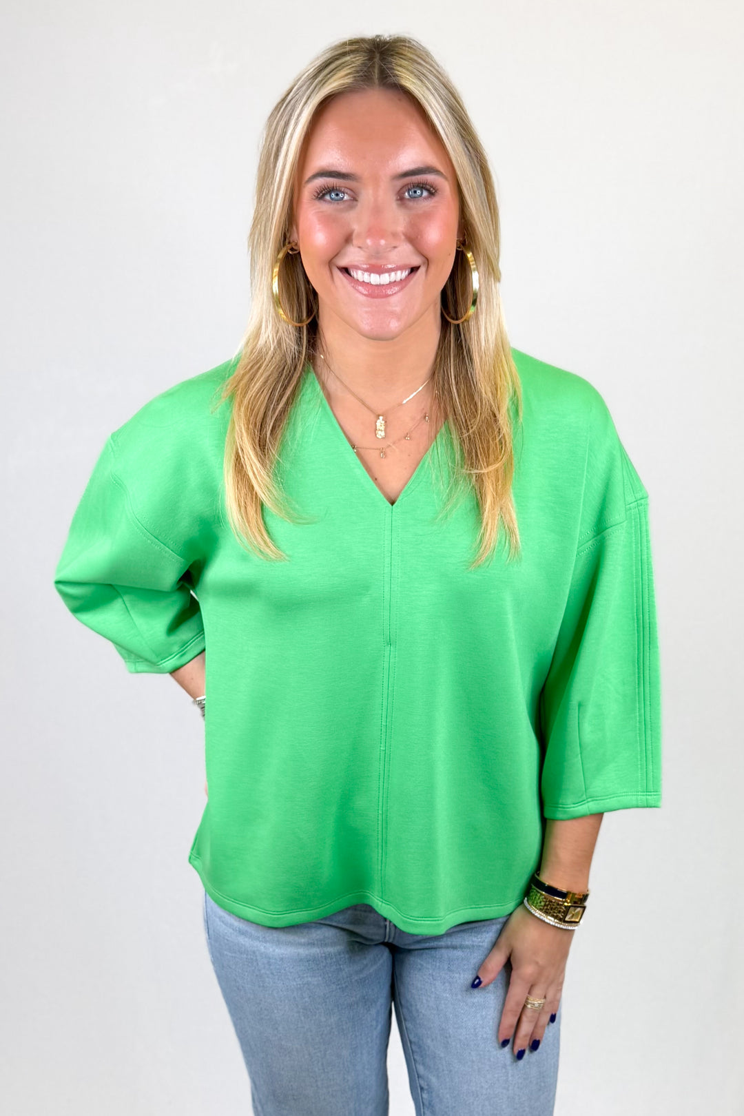 Woman wearing a bright green blouse and light blue jeans against a white background