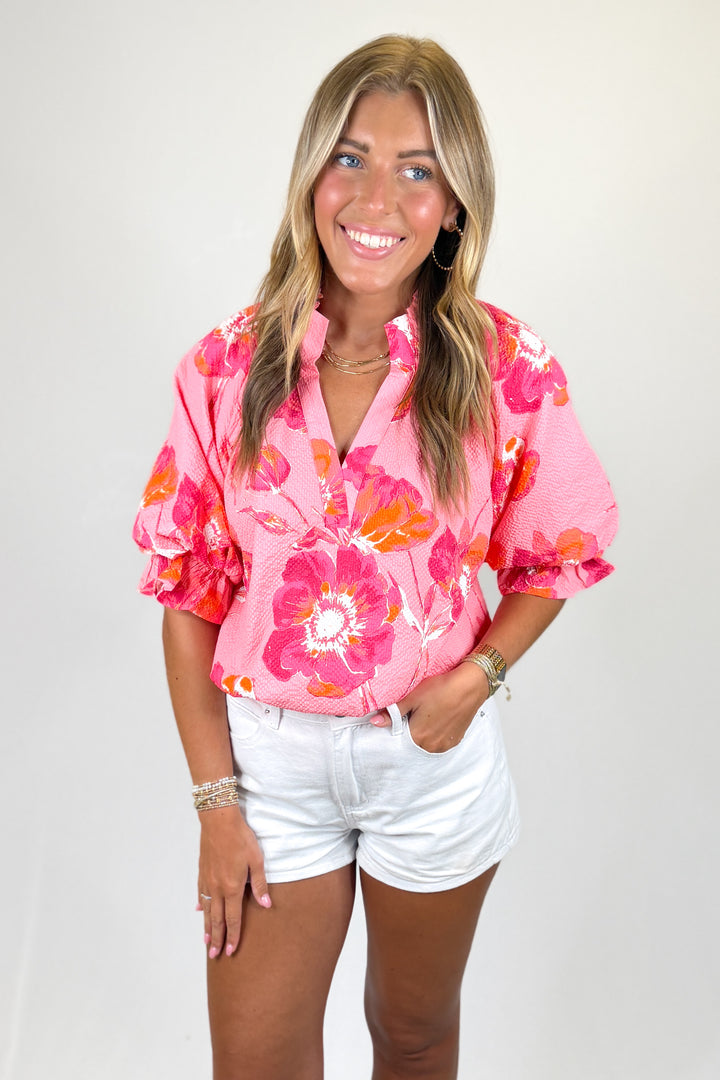 Woman wearing a pink floral blouse and white shorts on a plain background