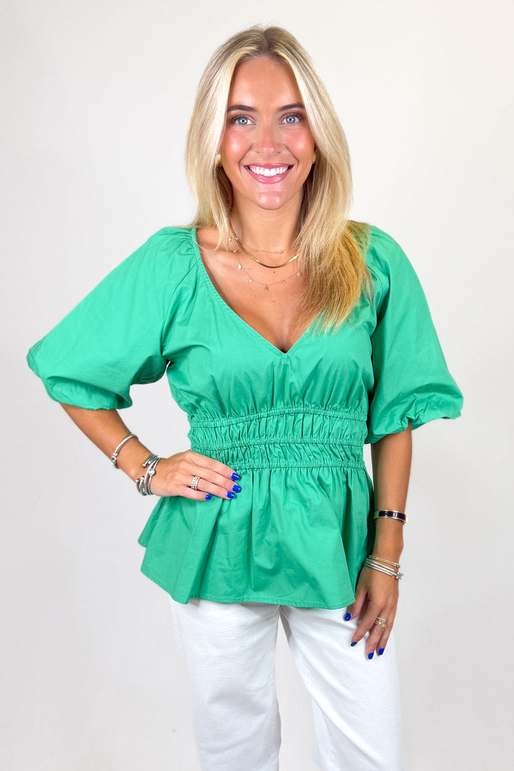 Woman wearing a green blouse and white pants against a plain background