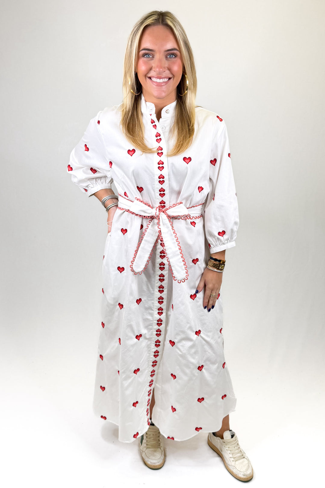 Woman wearing a white dress with red heart patterns on a plain background