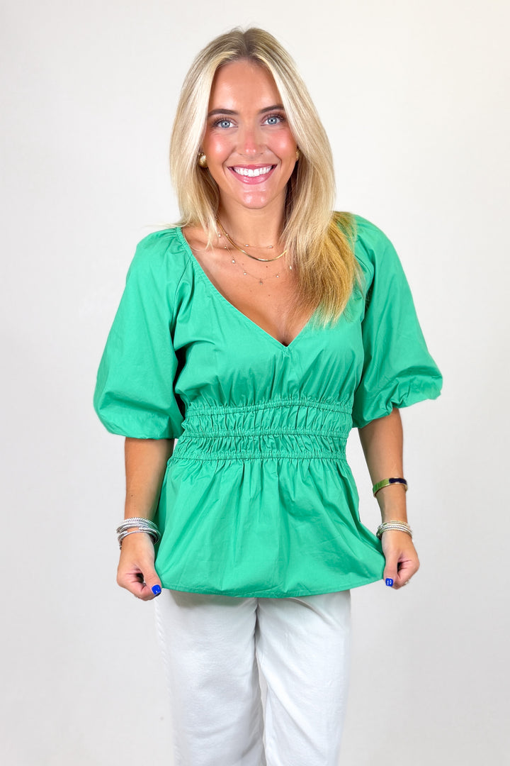 Woman wearing a green blouse and white pants against a plain background
