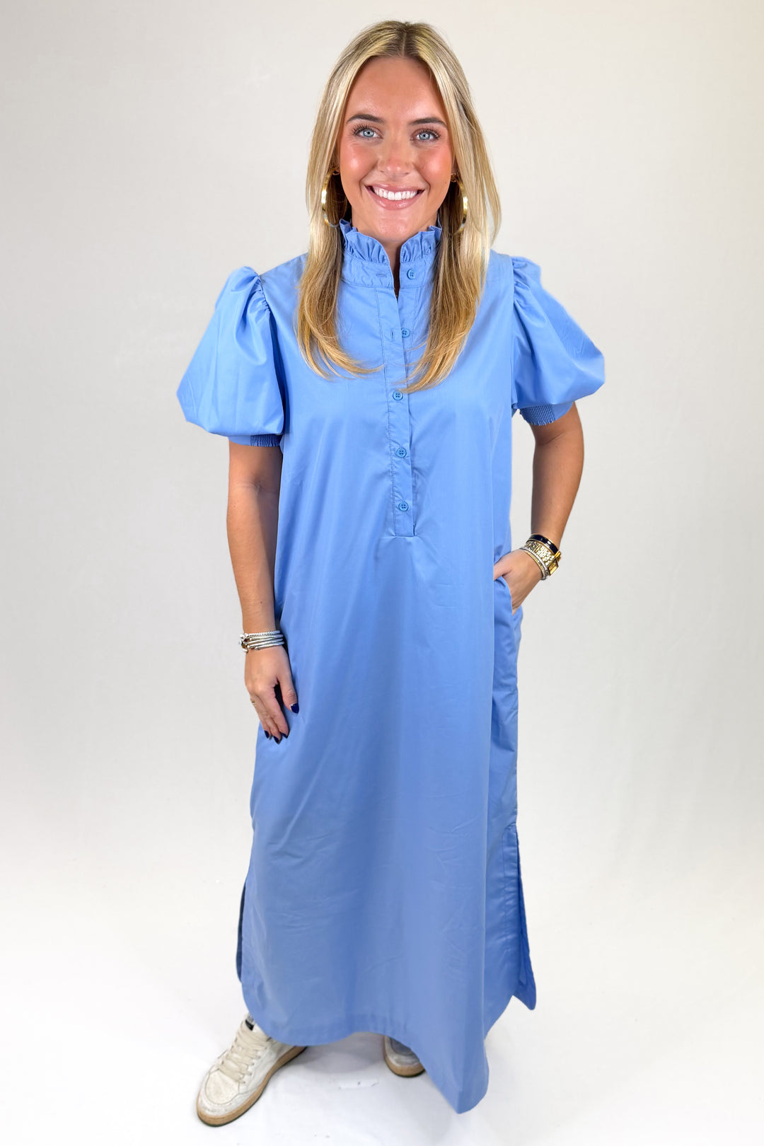 Woman wearing blue maxi dress with ruffle neck and puff sleeve against a plain background.