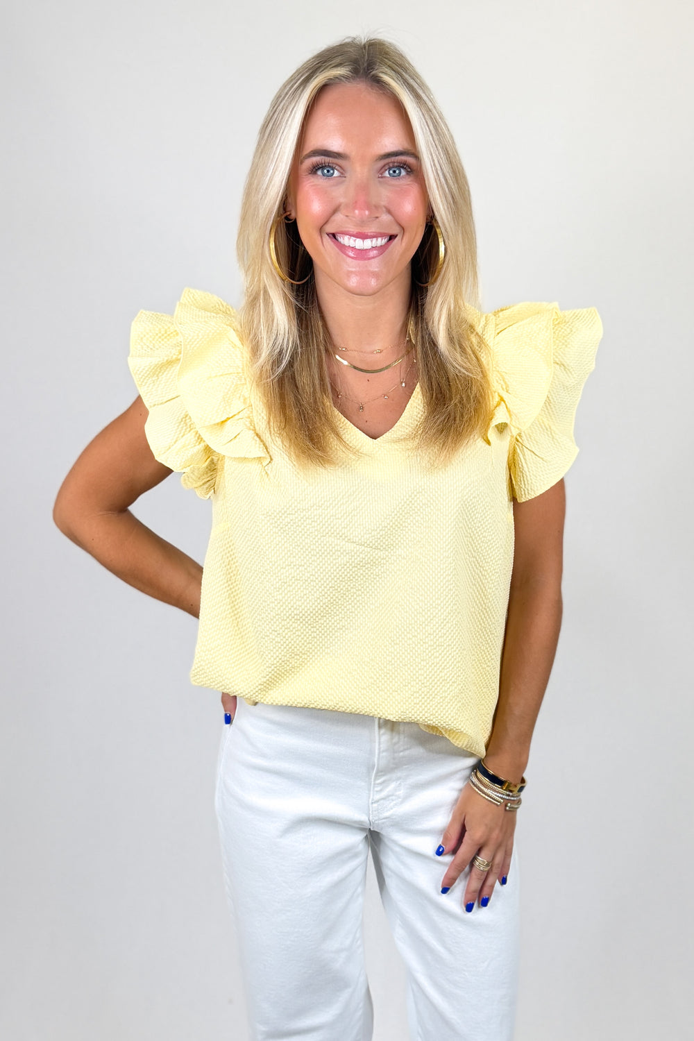 Woman wearing a yellow top with ruffled sleeves against a plain background