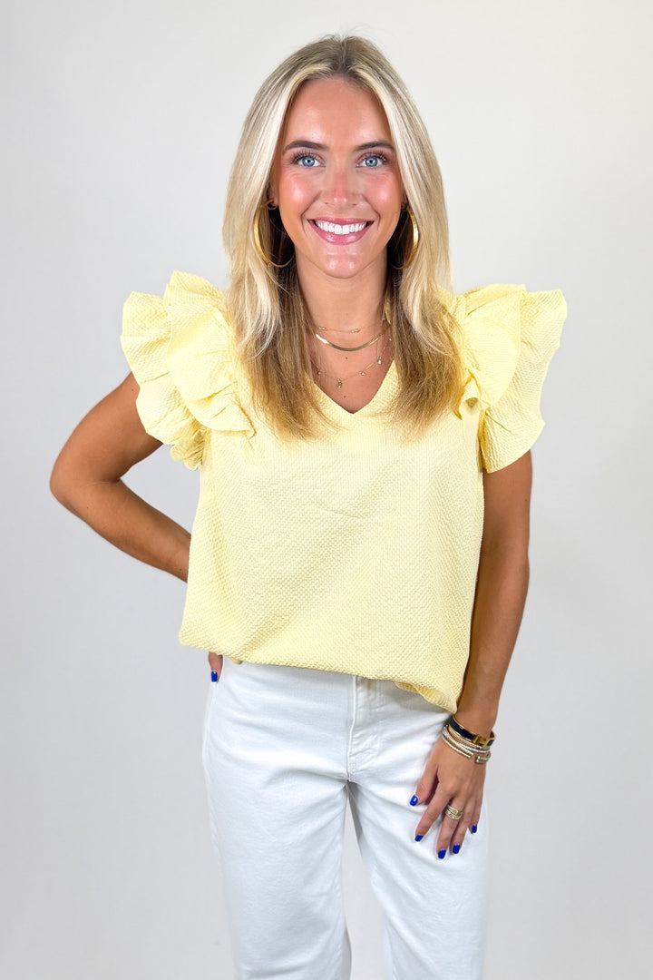 Woman wearing a yellow top with ruffled sleeves against a plain background