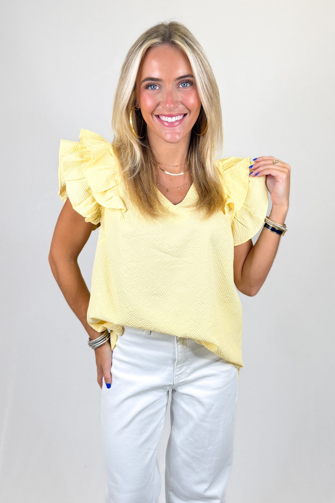 Woman wearing a yellow blouse with ruffled sleeves against a plain background