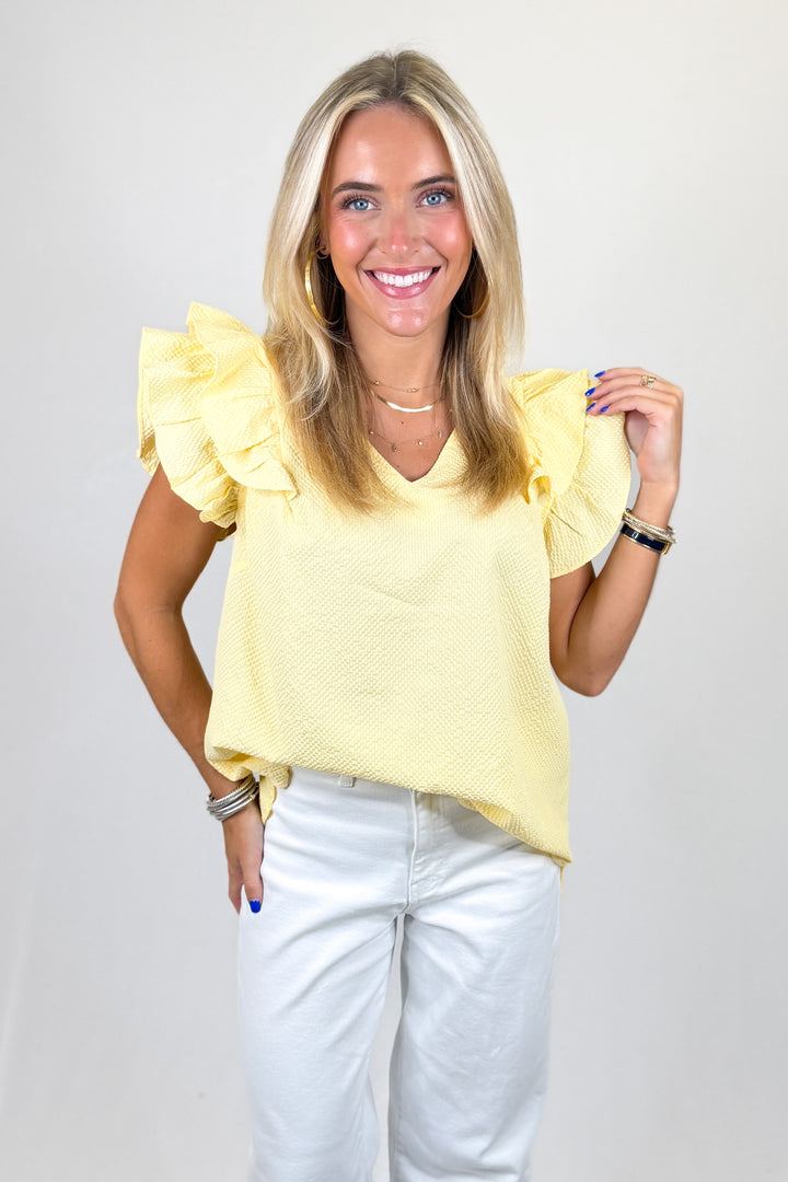 Woman wearing a yellow blouse with ruffled sleeves against a plain background