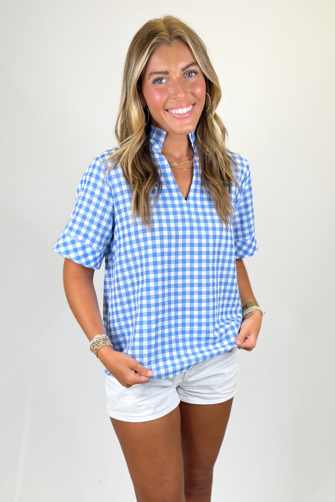 Woman wearing a blue and white checkered shirt and white shorts on a plain background