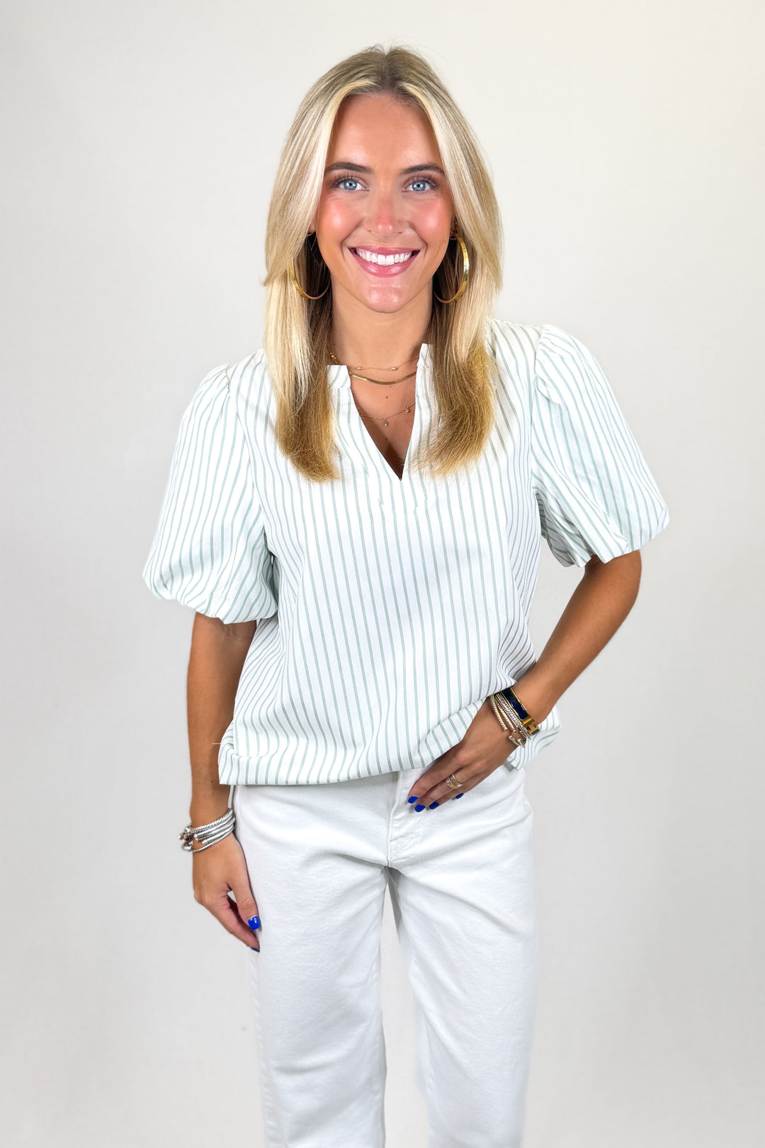 Woman wearing a light-colored ribbed sweater and white pants on a plain background
