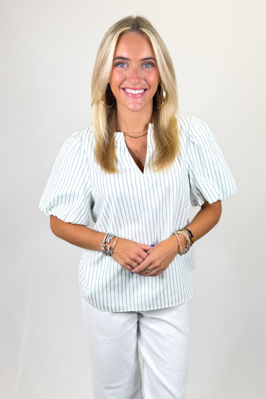 Woman wearing a striped shirt and white pants against a plain background