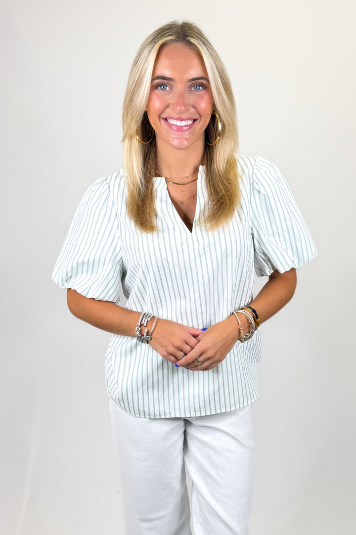Woman wearing a striped shirt and white pants against a plain background